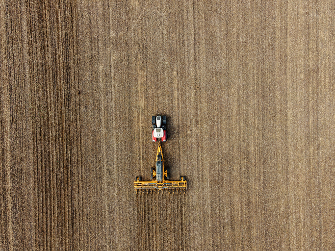 Aerial view of a tractor pulling a tillage implement across a harvested field
