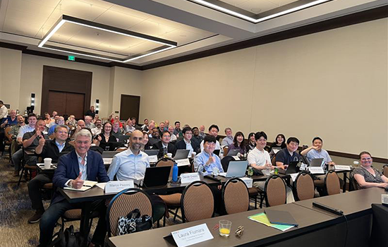 A group of professionals gathered in a conference room, sitting at rows of tables.