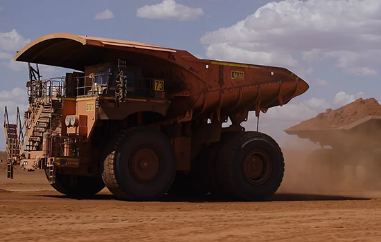 An autonomous mining truck hauls materials across a dusty dirt road